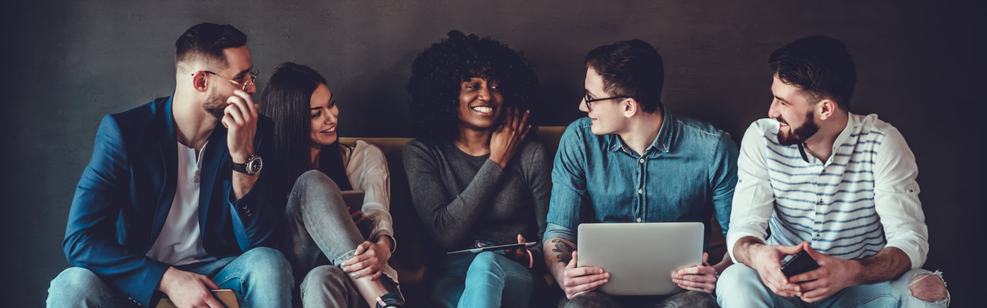 Happy diverse friends group sharing social media app news sitting holding phones, smiling multiracial young people students showing funny videos on laptop