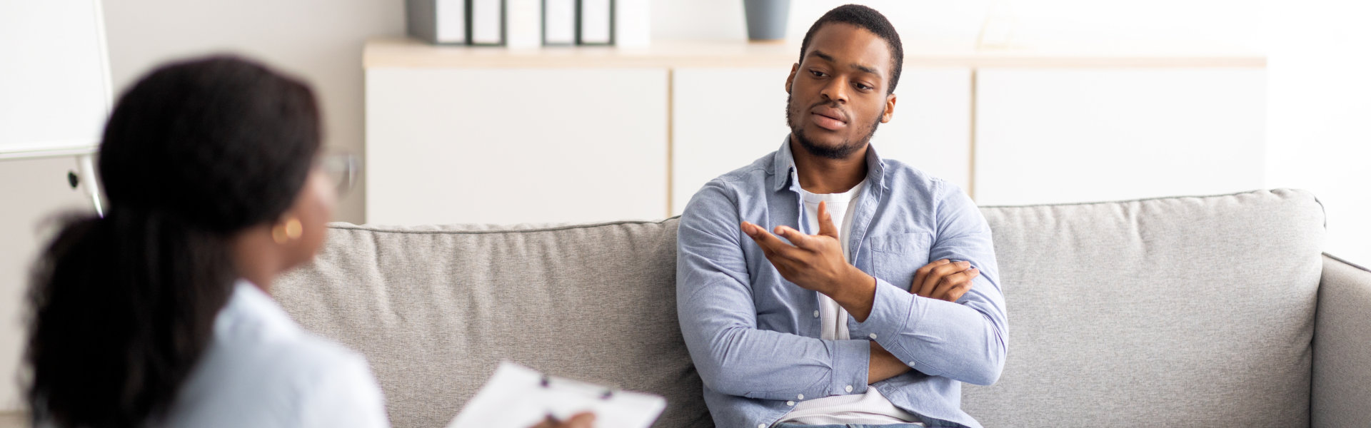 Professional psychologist helping black male patient, working with unhappy African American man, providing support and assistance at clinic